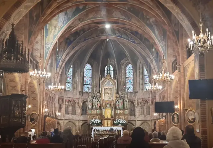 Wnętrze sanktuarium w Gietrzwałdzie, z ołtarzem głównym, witrażami i wiernymi na ławkach.