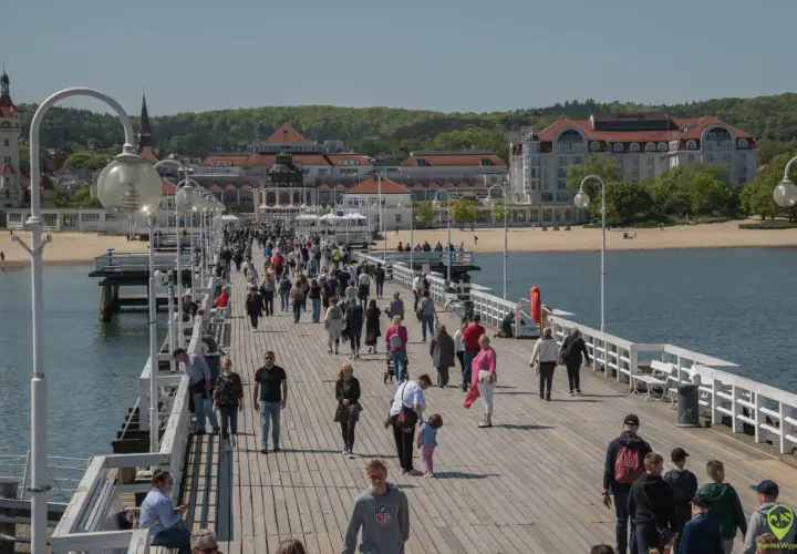 Tłum ludzi spaceruje po molo w Sopocie, jednym z najpopularniejszych gdańsk atrakcje. W tle widać plażę i zabytkowe budynki.