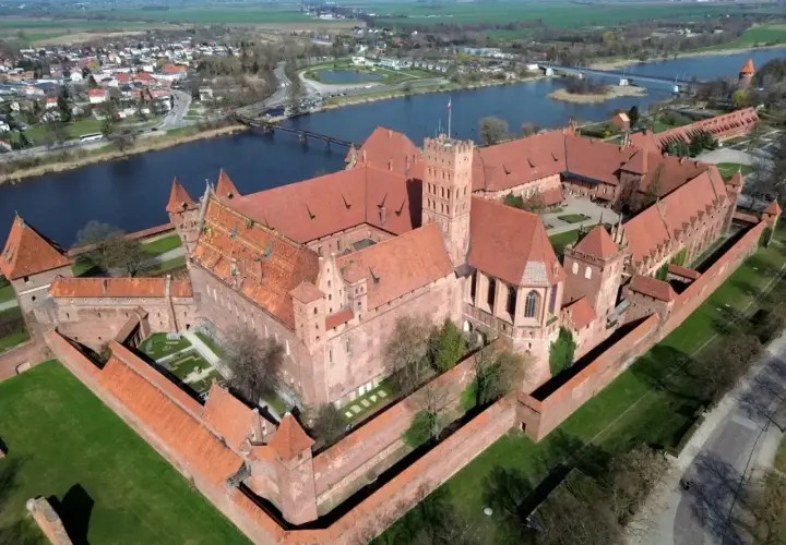 Potężny zamek w Malborku, jedna z największych atrakcji Polski, widziany z lotu ptaka. Rozległy kompleks z czerwonej cegły otoczony murami obronnymi, nad rzeką Nogat.