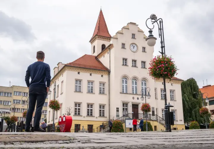 Mężczyzna podziwia ratusz w Trzebnicy, jedną z głównych atrakcji miasta. W tle czerwone serce i kwitnące kwiaty.