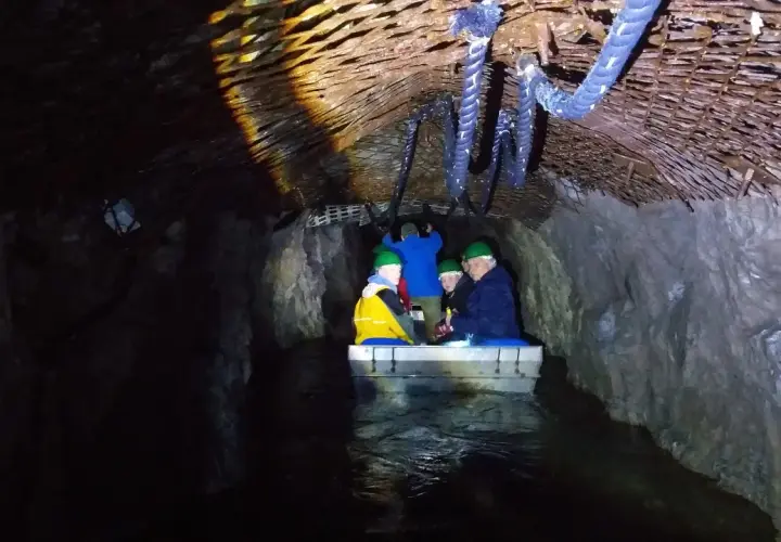 Podziemna łódź z turystami w kaskach płynie przez tunel. Czy to osówka czy włodarz, trudno stwierdzić w mroku.