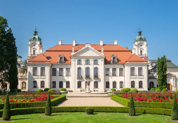 Pałac Zamoyskich w Kozłówce, z czerwonym dachem i wieżyczkami, otoczony kwitnącym ogrodem z czerwonymi różami.