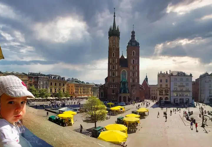 Małe dziecko na tle Rynku Głównego w Krakowie. Wspaniałe miejsce, by zobaczyć, co można robić w Krakowie: zwiedzać, spacerować, podziwiać architekturę.