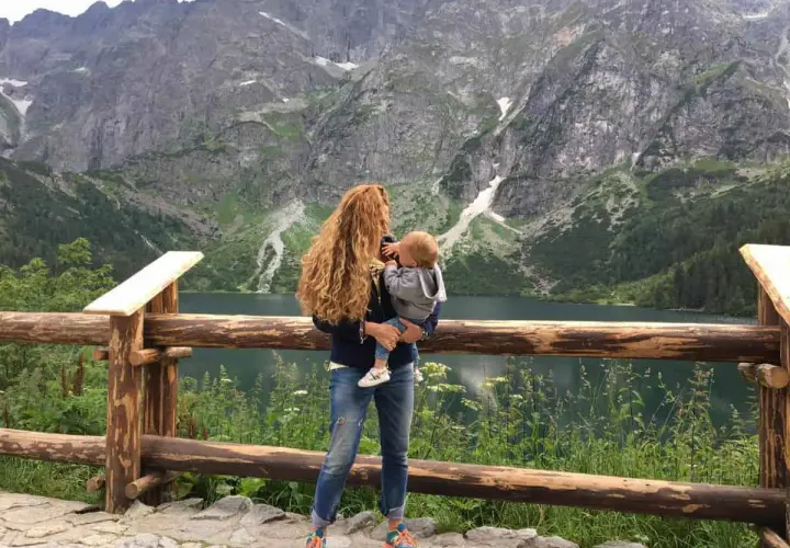 Kobieta z dzieckiem na rękach podziwia malowniczy widok Tatr. Wspaniałe **Zakopane z wózkiem** to idealne miejsce na rodzinne wycieczki.