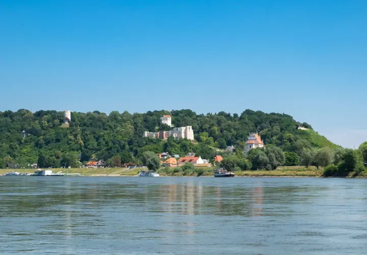Widok na zamek i miasteczko na wzgórzu, z rzeką i łodziami na pierwszym planie. Kazimierz Dolny trasa zachwyca.