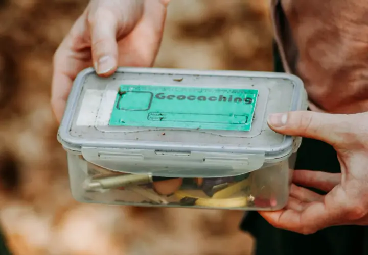 Pudełko z napisem "Geocaching" i drobiazgami w środku. To świetna zabawa, która polega na szukaniu ukrytych skarbów.