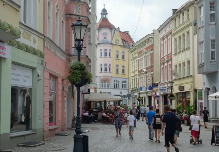 Kolorowa ulica z kamienicami, latarnią i ludźmi spacerującymi po deptaku. Zielona Góra oferuje wiele atrakcji.