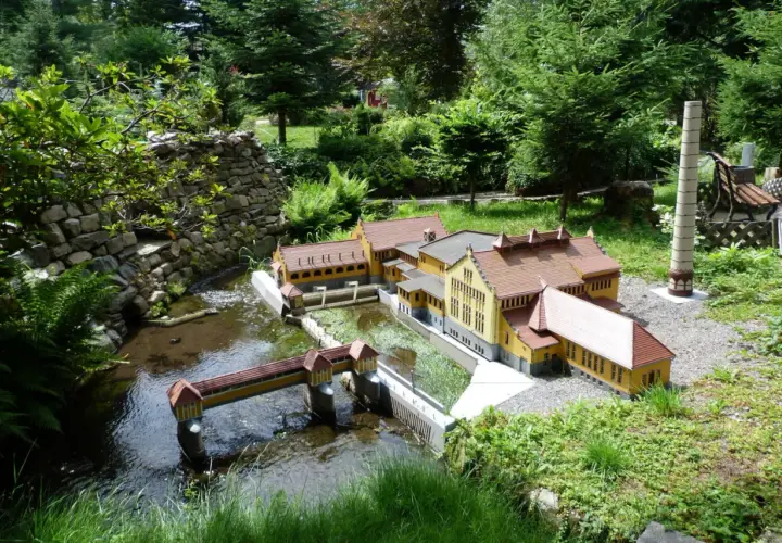 Miniaturowa zabudowa z mostkiem i rzeką, jak w parkach miniatur w Polsce.