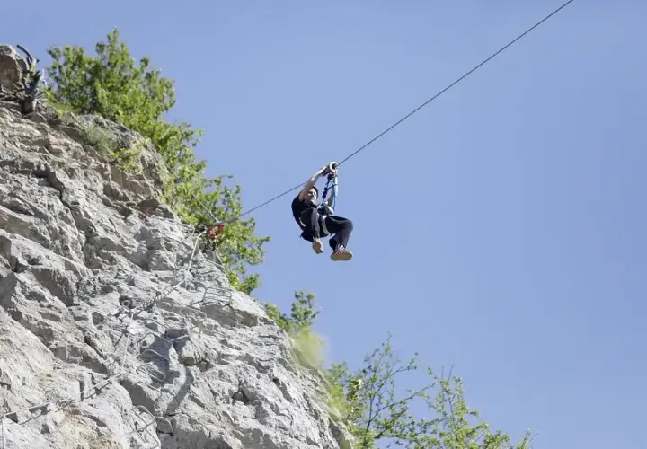 Człowiek zjeżdża na tyrolce obok skalnej ściany z ubezpieczeniami, jak na via ferrata polska.