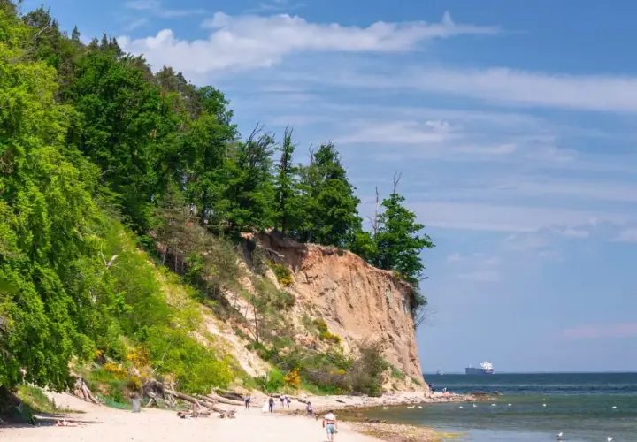 Piękny klif i plaża, idealne atrakcje nad morzem. Ludzie spacerują, odpoczywają, a na horyzoncie widać statek.