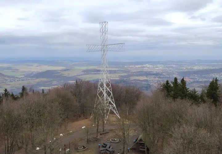 Wielki metalowy krzyż góruje nad lasem na **chełmiec szczyt**. W oddali rozciąga się panorama miasta i pagórkowatego krajobrazu.