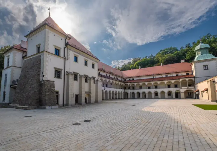Zamek w Suchej Beskidzkiej z dziedzińcem i arkadowymi krużgankami. W tle zielone wzgórza.