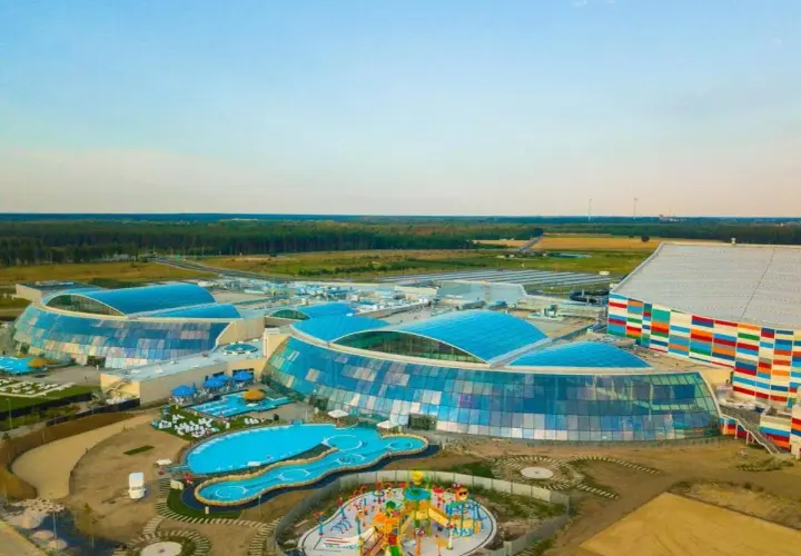 Największy aquapark w Polsce z błękitnymi, szklanymi dachami i kolorową fasadą, otoczony zielenią i basenami.