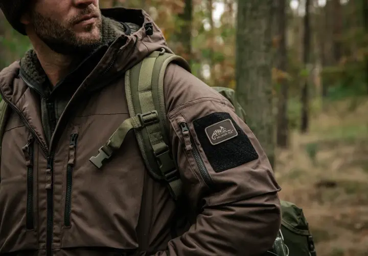 Mężczyzna w brązowej kurtce z naszywką Helikon-Tex, gotowy na przygodę. To dowód, że polskie marki outdoorowe to jakość i styl.