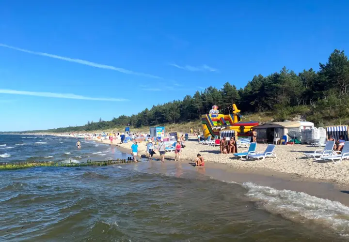 Plaża w Grzybowie pełna życia: dmuchany zamek, leżaki i tłumy plażowiczów cieszących się słońcem.
