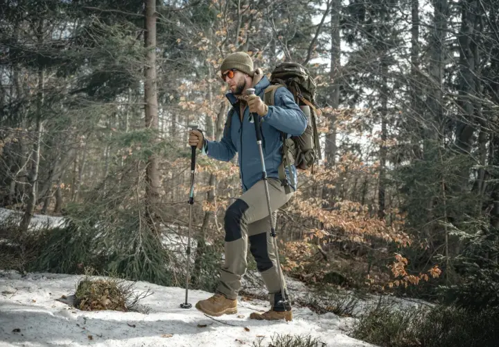 Mężczyzna z plecakiem i kije trekkingowe przemierza ośnieżony las.