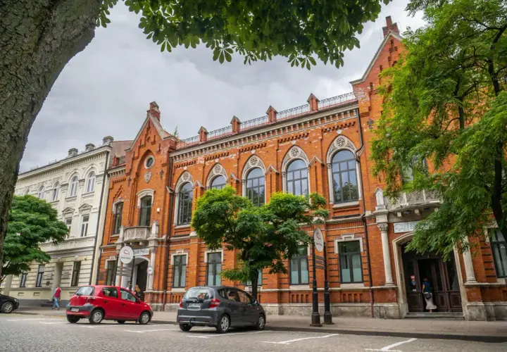 Kamienice w Radomiu, w tym Bank Polski, to ciekawe **radom atrakcje**. Dwa samochody zaparkowane na brukowanej ulicy.