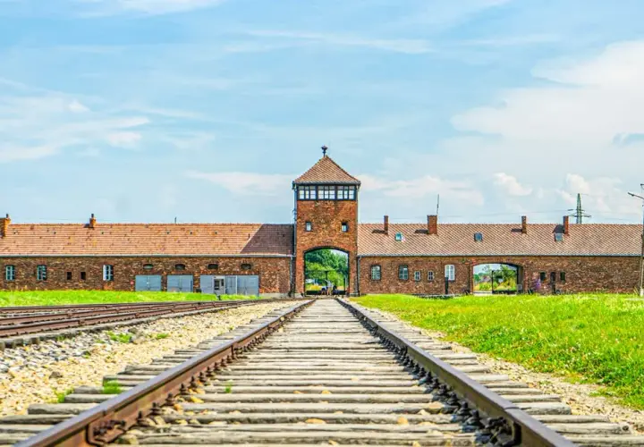 Brama obozowa w Oświęcimiu, z torami kolejowymi prowadzącymi do niej. Miejsce pamięci, które jest ważną częścią historii i atrakcją turystyczną.