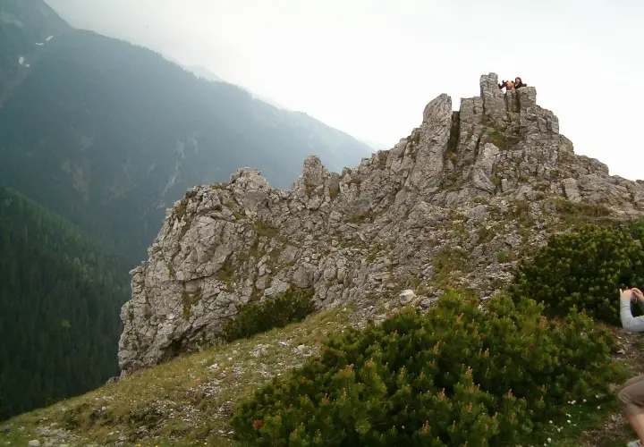 Sarnia góra wznosi się dumnie, skaliste szczyty przyciągają wzrok. Na górze widać ludzi podziwiających panoramę.