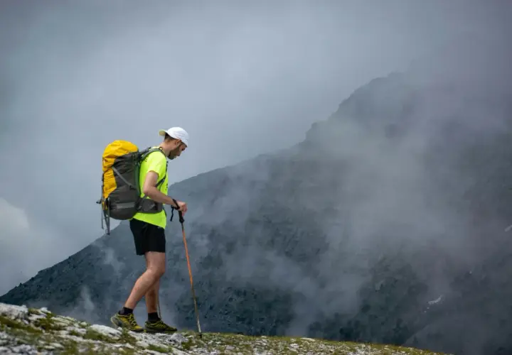 Mężczyzna z plecakiem i kijkami trekkingowymi wchodzi na mglisty szczyt. Wspaniały wyjazd w góry!