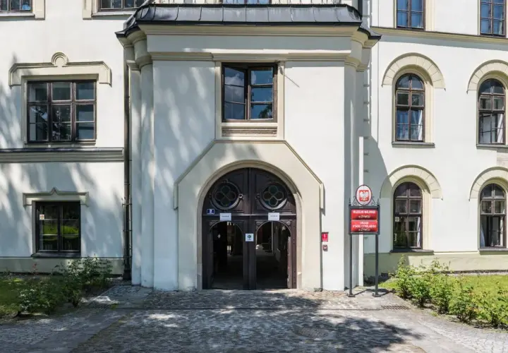 Wejście do zabytkowego zamku w Żywcu, z charakterystycznymi drzwiami i oknami. Obok tablica informująca o Muzeum Miejskim i Urzędzie Stanu Cywilnego.