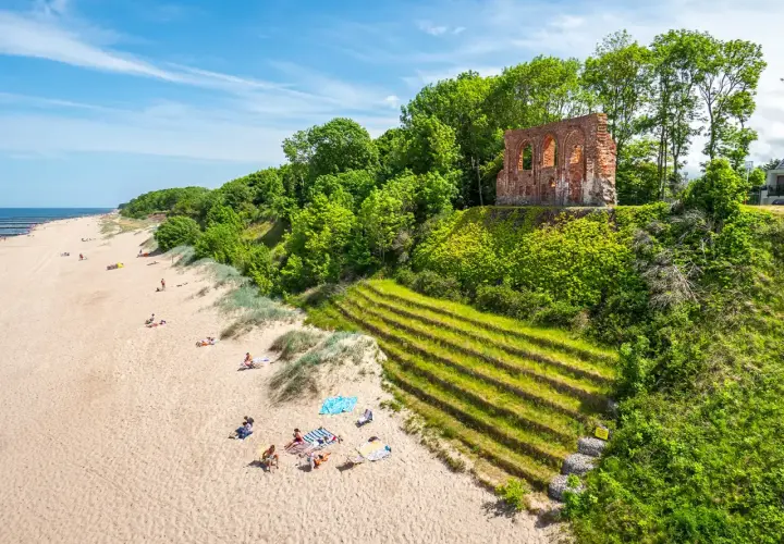 Piękna plaża z ruinami na wzgórzu, zielone zbocza i ludzie odpoczywający na piasku. Trzęsacz atrakcje zachwycają!