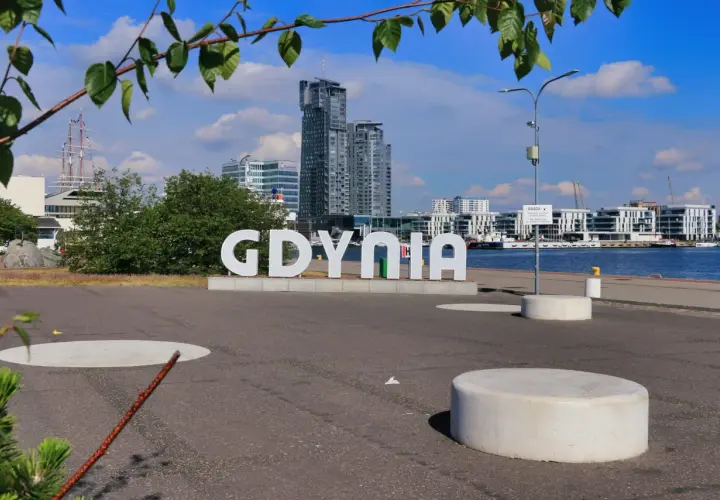 Napis GDYNIA na tle nowoczesnej architektury i żaglowca. Widok z Gdynia Rynek Główny.