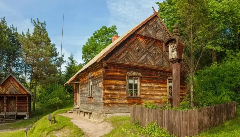 Drewniane chaty i kapliczka na słupie w jednym z urokliwych skansenów w Polsce.