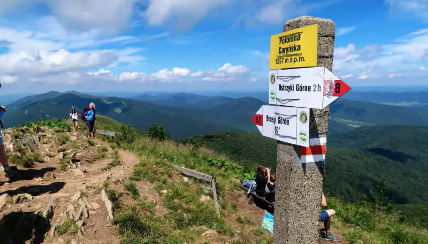 Widok na Połoninę Caryńską, gdzie zaczynają się Bieszczady. Szlak turystyczny, znaki kierunkowe i odpoczywający turyści.