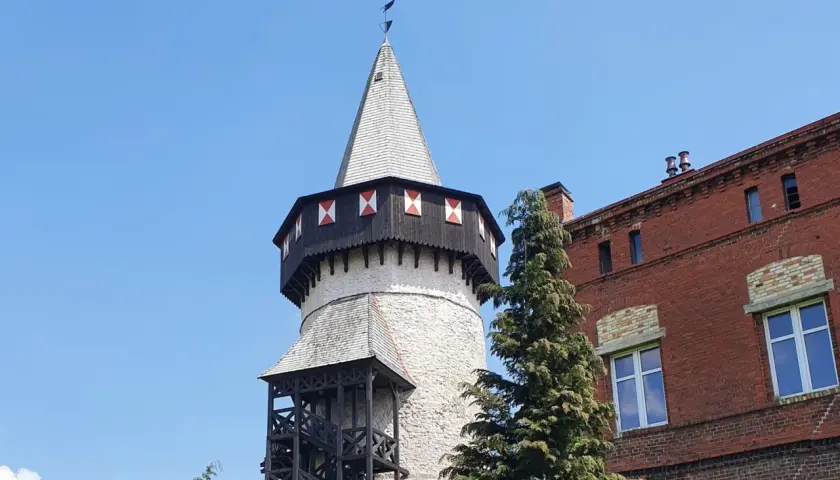 Wieża zamkowa w Prudniku, jedna z głównych atrakcji, z ptakiem w locie na tle błękitnego nieba.