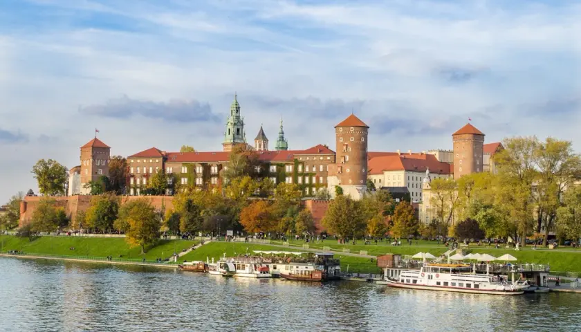 Kraków, miasto nad Wisłą, z Wawelem w jesiennej odsłonie. Statki wycieczkowe cumują przy brzegu.