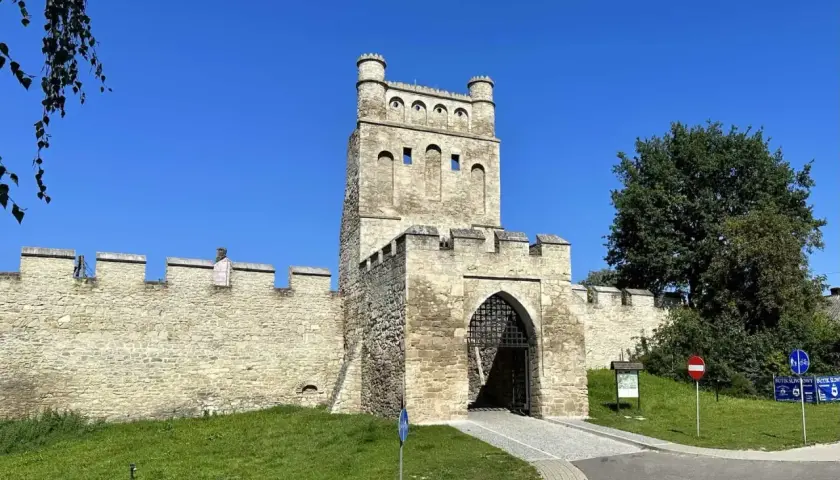Kamienna brama z wieżą i murami obronnymi, jak z polskiego Carcassonne, w słoneczny dzień.
