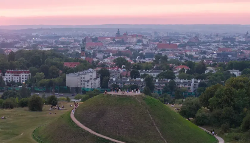 Zachód słońca nad Krakowem, z Kopcem Kraka na pierwszym planie, gdzie spacerują ludzie.