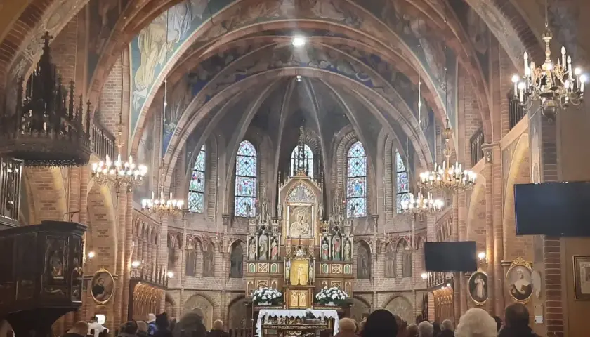 Wnętrze sanktuarium w Gietrzwałdzie, z ołtarzem głównym, witrażami i wiernymi na ławkach.