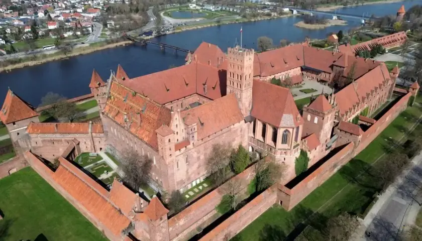 Potężny zamek w Malborku, jedna z największych atrakcji Polski, widziany z lotu ptaka. Rozległy kompleks z czerwonej cegły otoczony murami obronnymi, nad rzeką Nogat.