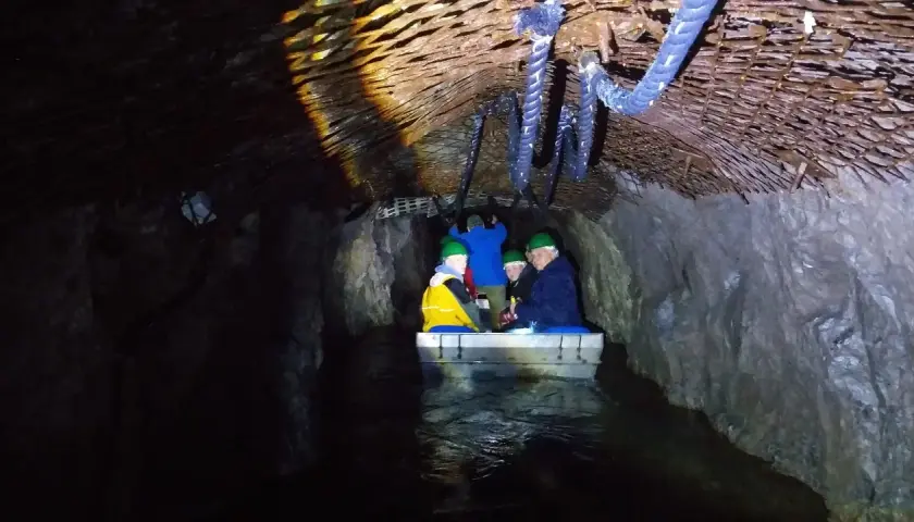 Podziemna łódź z turystami w kaskach płynie przez tunel. Czy to osówka czy włodarz, trudno stwierdzić w mroku.