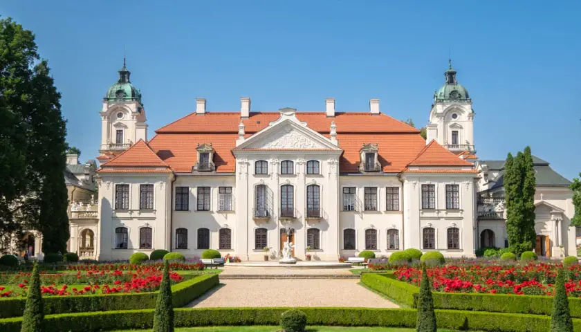Pałac Zamoyskich w Kozłówce, z czerwonym dachem i wieżyczkami, otoczony kwitnącym ogrodem z czerwonymi różami.