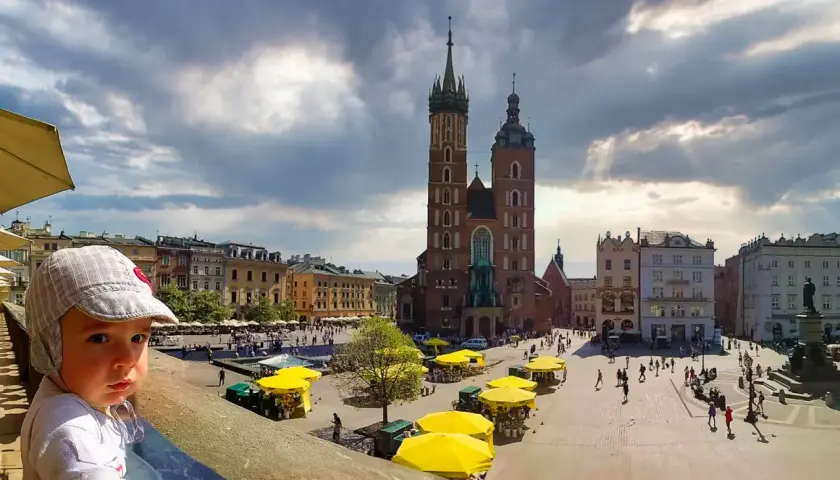 Małe dziecko na tle Rynku Głównego w Krakowie. Wspaniałe miejsce, by zobaczyć, co można robić w Krakowie: zwiedzać, spacerować, podziwiać architekturę.