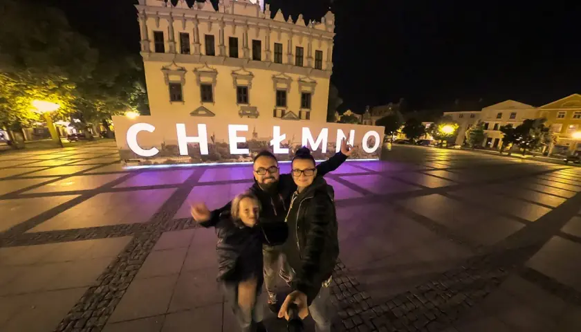 Rodzina pozuje do zdjęcia na tle napisu "Chełmno" i ratusza nocą.