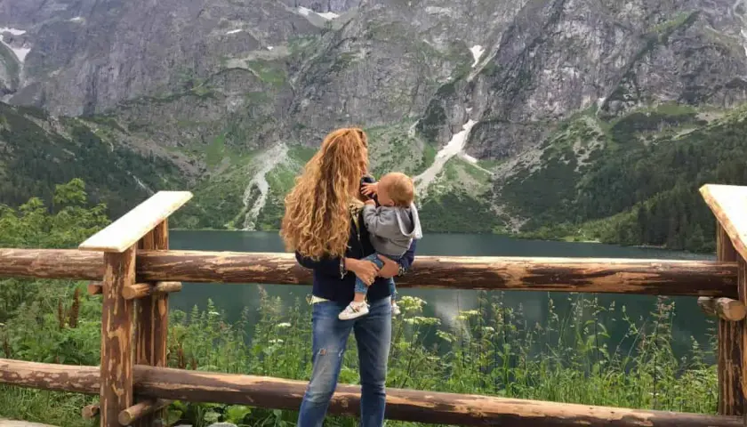 Kobieta z dzieckiem na rękach podziwia malowniczy widok Tatr. Wspaniałe **Zakopane z wózkiem** to idealne miejsce na rodzinne wycieczki.