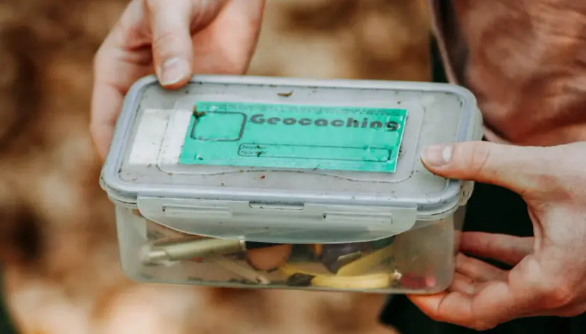 Pudełko z napisem "Geocaching" i drobiazgami w środku. To świetna zabawa, która polega na szukaniu ukrytych skarbów.