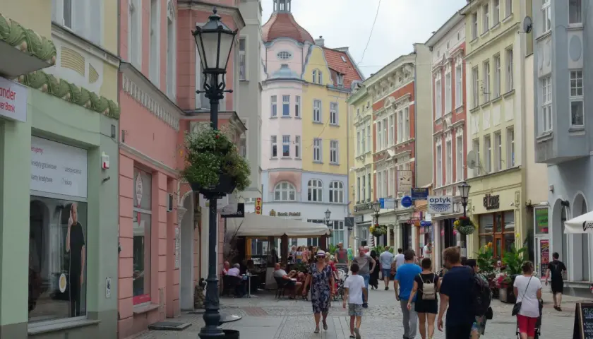 Kolorowa ulica z kamienicami, latarnią i ludźmi spacerującymi po deptaku. Zielona Góra oferuje wiele atrakcji.