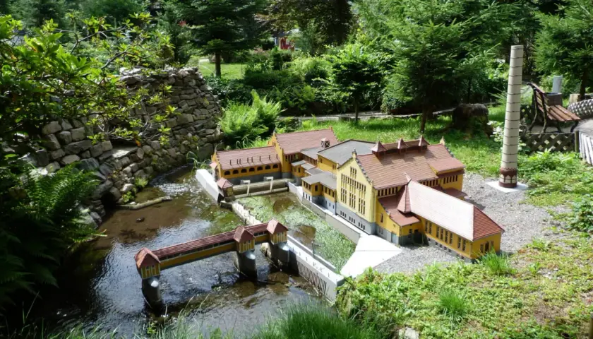 Miniaturowa zabudowa z mostkiem i rzeką, jak w parkach miniatur w Polsce.