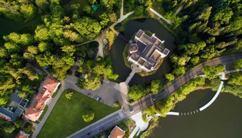 Zamek w Kórniku otoczony fosą i parkiem, widziany z lotu ptaka. Malowniczy krajobraz z drogą i budynkami w tle.