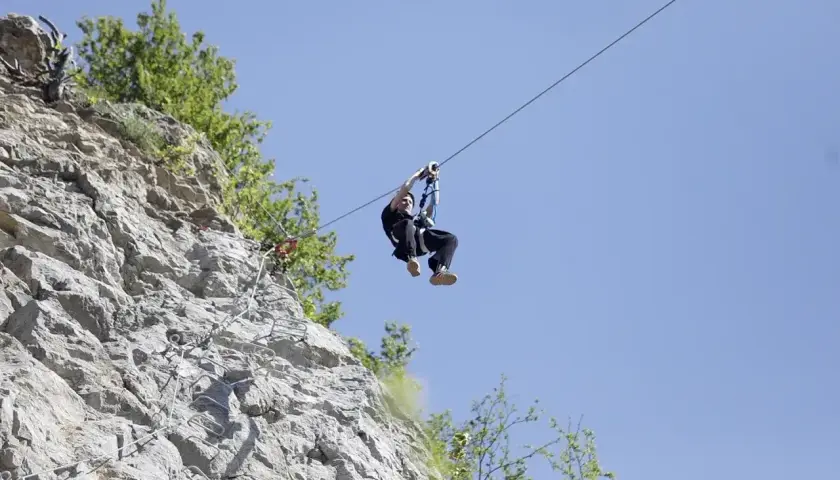 Człowiek zjeżdża na tyrolce obok skalnej ściany z ubezpieczeniami, jak na via ferrata polska.