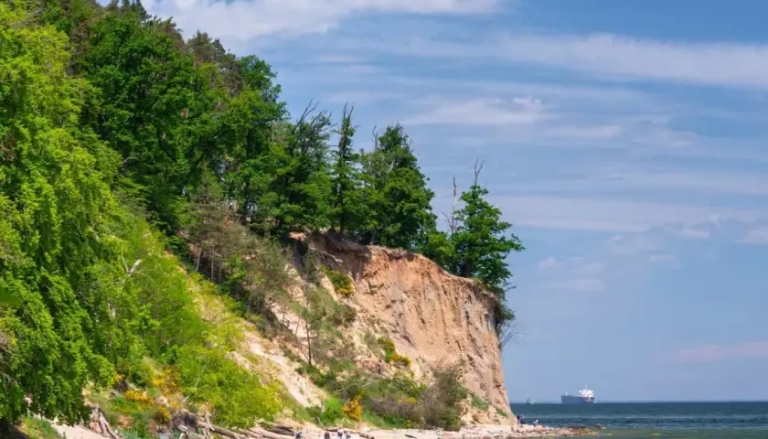 Piękny klif i plaża, idealne atrakcje nad morzem. Ludzie spacerują, odpoczywają, a na horyzoncie widać statek.