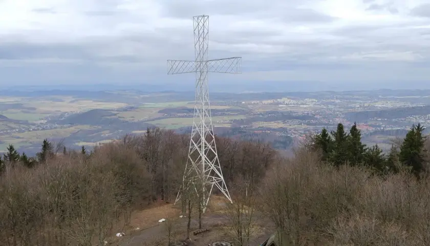 Wielki metalowy krzyż góruje nad lasem na **chełmiec szczyt**. W oddali rozciąga się panorama miasta i pagórkowatego krajobrazu.