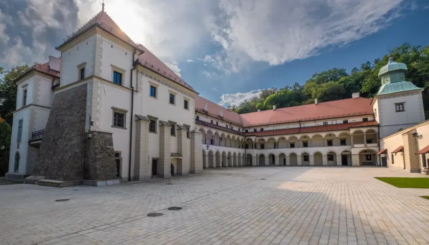 Zamek w Suchej Beskidzkiej z dziedzińcem i arkadowymi krużgankami. W tle zielone wzgórza.