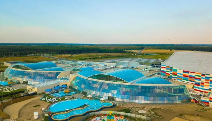 Największy aquapark w Polsce z błękitnymi, szklanymi dachami i kolorową fasadą, otoczony zielenią i basenami.