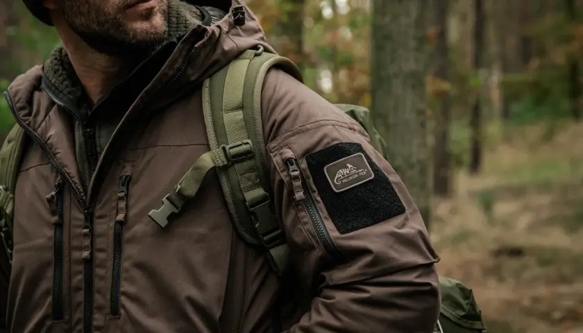 Mężczyzna w brązowej kurtce z naszywką Helikon-Tex, gotowy na przygodę. To dowód, że polskie marki outdoorowe to jakość i styl.